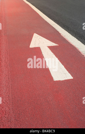 Tout droit en direction de la flèche blanche peinte sur une surface de la route rouge vif Banque D'Images