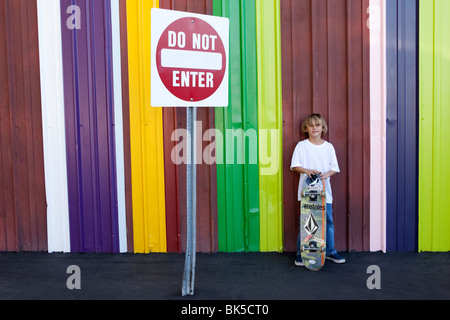 Garçon avec skateboard en face de mur à rayures colorées Banque D'Images