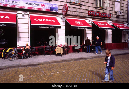 Garçon joue sur la rue en face de 'Costa' café café avec un coin salon extérieur. Banque D'Images