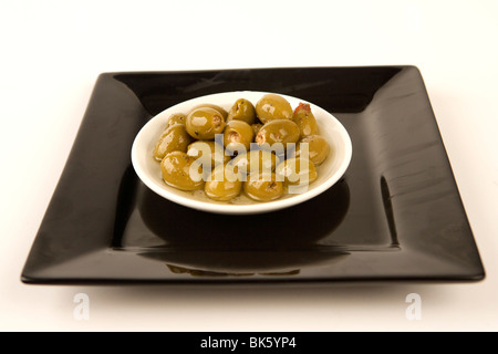 Un bol d'olives vertes dans un bol blanc sur une plaque noire sur fond blanc Banque D'Images