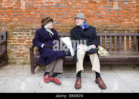 Un couple de personnes âgées venez déguster un sandwich déjeuner sur un banc dans les jardins du Palais de l'évêque, Chichester, West Sussex, Angleterre. Banque D'Images