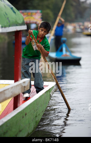 Un garçon utilise un poteau pour naviguer son bateau à travers le canal de Xochimilco, au sud de la ville de Mexico Banque D'Images