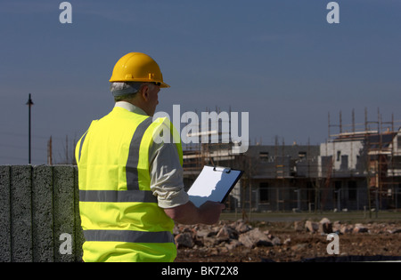 L'homme aux cheveux gris d'âge moyen wearing hard hat et hivis vest tenant un presse-papiers sur chantier de construction Banque D'Images