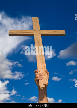 La main d'un homme tenant une croix en bois haut dans le ciel. Banque D'Images