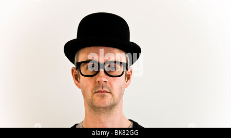 Homme d'âge moyen avec une expression sérieuse dans un chapeau de melon et de grandes lunettes regardant l'appareil photo. Concept de l'humour Banque D'Images