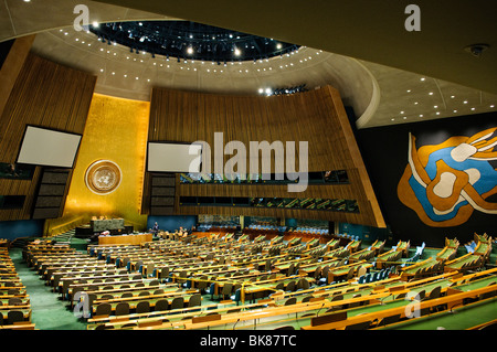 Intérieur de la salle de l'Assemblée générale des Nations Unies New York // NEW YORK, New York — intérieur de la salle de l'Assemblée générale des Nations Unies au siège des Nations Unies. La vaste salle circulaire présente des rangées de bureaux de délégués, un mur doré proéminent avec l'emblème de l'ONU et une fresque abstraite distinctive, créant un cadre grandiose pour la diplomatie internationale. Banque D'Images
