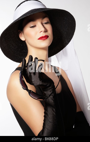 Jeune femme portant un chapeau noir et une robe noire lunettes tenant dans sa main et regardant vers le bas Banque D'Images