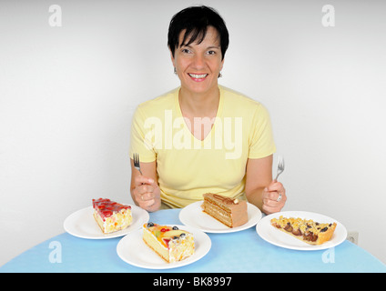 Femme assise heureusement en face de quatre plaques avec gâteau Banque D'Images