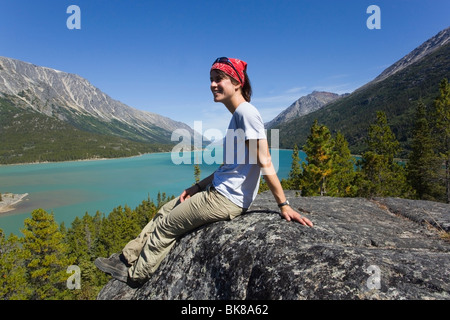 Jeune femme, randonneur, backpacker sitting on rock, se reposer, profiter de panorama sur le lac Bennett, le col Chilkoot, lieu historique Banque D'Images