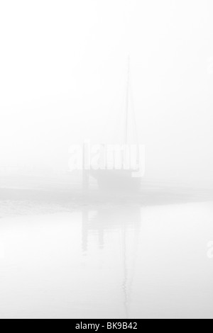 Un bateau amarré à marée basse sur la photo dans la brume matinale, à West Mersea, Essex Banque D'Images