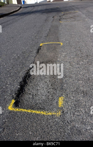 Poule au milieu d'une route bitumée au Royaume-Uni causée par les dégâts de gel par temps froid a marqué pour la réparation avec la peinture jaune Banque D'Images