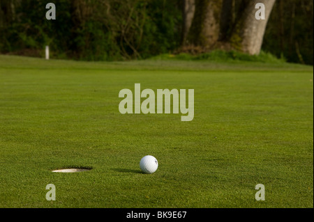 Une balle de golf se trouve à court de la droite du trou sur le green près du drapeau. Banque D'Images