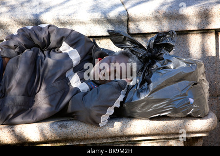 Sans-abri dormant sur un banc à l'aide de ses affaires comme un oreiller. Prospect Park, Brooklyn, New York. Banque D'Images