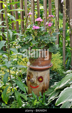 Géranium (pelargonium) sur une souche d'arbre avec un visage peint. design : Jutta wahren Banque D'Images