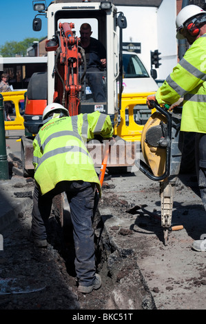 Ouvriers à l'aide d'un dispositif pneumatique essence, au Royaume-Uni. Les hommes travaillent avec des casques & ear defenders creuser jusqu'à la route. Banque D'Images