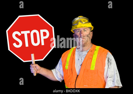 Une sale, grunge, travailleur de la construction de l'utilitaire grasse avec casque, gilet orange et des lunettes de protection est titulaire d'un panneau d'arrêt. Banque D'Images