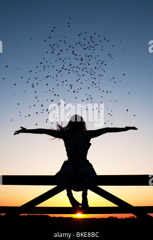 Jeune fille s'amusant avec les étoiles assis sur une barrière au coucher du soleil. Silhouette Banque D'Images