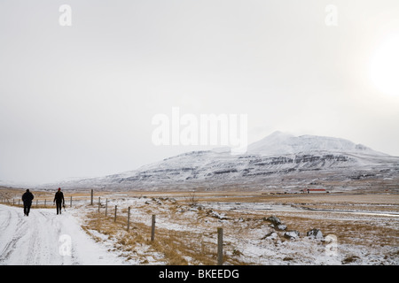 Deux personnes à pied sur une route dans le paysage enneigé. Islande Skagafjordur Banque D'Images