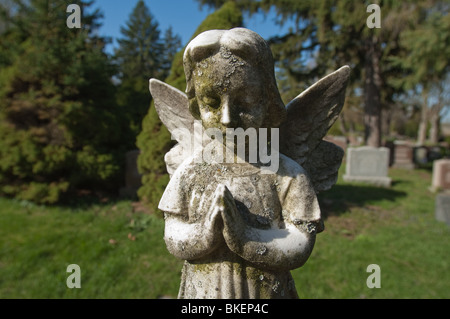 Une statue d'un enfant angélique est figée dans le temps avec ses' les mains jointes en prière silencieuse. Banque D'Images