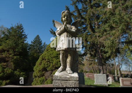 Une statue d'un enfant angélique est figée dans le temps avec ses' les mains jointes en prière silencieuse. Banque D'Images