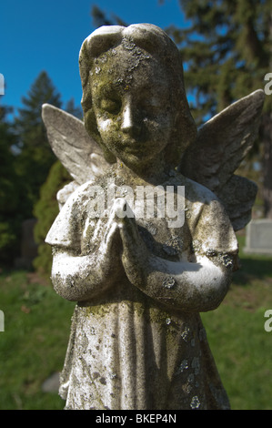 Une statue d'un enfant angélique est figée dans le temps avec ses' les mains jointes en prière silencieuse. Banque D'Images