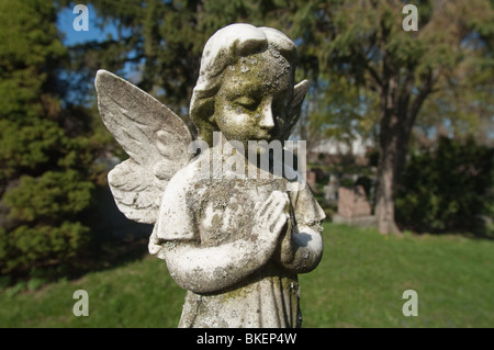 Une statue d'un enfant angélique est figée dans le temps avec ses' les mains jointes en prière silencieuse. Banque D'Images