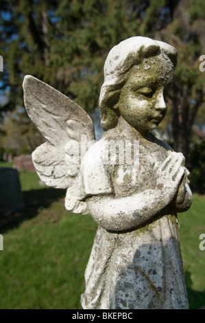 Une statue d'un enfant angélique est figée dans le temps avec ses' les mains jointes en prière silencieuse. Banque D'Images