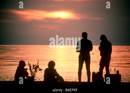 Deux couples pique-nique sur la plage en regardant le coucher de soleil et le partage de la nourriture Banque D'Images