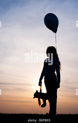 Silhouette d'une jeune fille tenant un ballon et d'un ours au coucher du soleil Banque D'Images