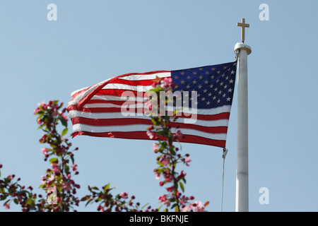 L'église catholique avec une croix et le drapeau américain sur un mât de drapeau avec l'arbre en fleurs contre le ciel bleu angle bas personne horizontal dans l'Ohio USA US h-RES Banque D'Images