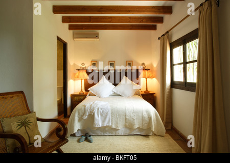 Les lampes allumées sur les tables de chevet de chaque côté du lit avec coussins crème et crème double-couverture en poutres apparentes chambre espagnole Banque D'Images