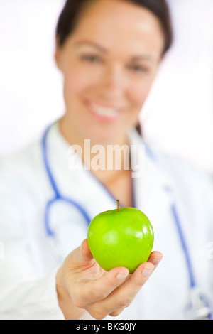 La saine alimentation ou de style concept tourné of a smiling woman doctor holding et offrant une pomme verte Banque D'Images