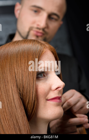 Coiffeur professionnel avec de longs cheveux rouges fashion model au salon de luxe noir Banque D'Images