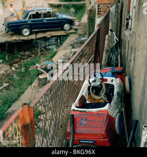 Bien-utilisé voiture jouet stockés sur balcon de maison délabrée et un vrai bleu Trabant à l'ancienne voiture garée à l'arrière-plan Banque D'Images