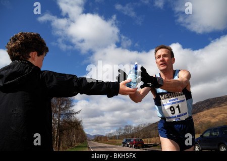 Marathon de Lochaber organisée chaque année par le loch linnie.Runner atteint pour un peu d'eau au cours de la race,de jeune garçon.Sunshine Banque D'Images