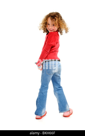 Fillette de six ans avec une dent de devant porter un jean bleu et une chemise rouge avec des sandales pose pour la caméra Banque D'Images