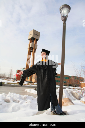 Carefree smiling blonde woman in graduation sur le campus uniforme holding diploma vue pleine longueur Banque D'Images