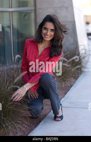 Une belle jeune femme indienne (de l'Est) est accroupi sur le sol près d'un trottoir, souriant. Banque D'Images