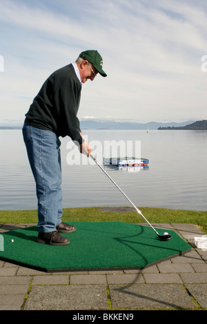 Golfeur se prépare à frapper la plate-forme balle de golf vers flottant sur le lac, Taupo, Nouvelle-Zélande Banque D'Images