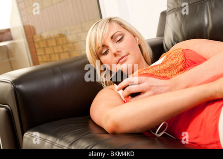 Femme blonde à l'écoute de i pod allongé sur le canapé Banque D'Images