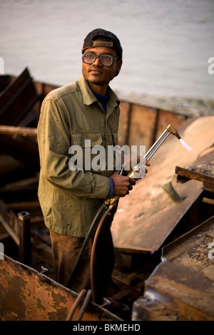 Un homme démantèle un bateau avec un chalumeau et d'un marteau sur les rives de la rivière Karnaphuli sous le pont, Kalurghat Chittago Banque D'Images