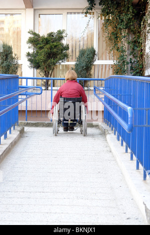 Femme handicapée sur fauteuil roulant d'entrer dans le bâtiment à l'aide de rampe pour personnes à mobilité réduite Banque D'Images