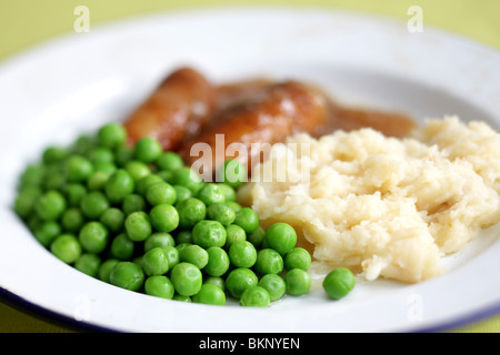 Réchauffement britannique traditionnel confort alimentaire de saucisses de porc avec de la purée de pommes de terre, petits pois et sauce servi sur une plaque avec aucun peuple Banque D'Images