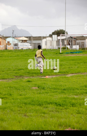 Boy kicking soccer ball dans le Township Banque D'Images