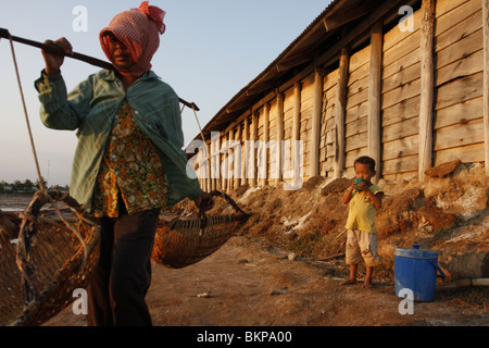 Un enfant accompagne sa mère qui travaille dans le sel chaud scorchingly de fermes de Kampot, au Cambodge. Banque D'Images