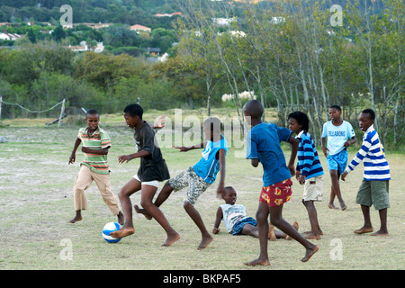 Les enfants africains jouant au football pieds nus dans un champ à Hout Bay, à Cape Town, Afrique du Sud. Banque D'Images