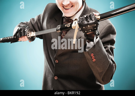 Young smiling businessman with épée dans ses bras prêts à se battre avec ses rivaux et de gagner. L'entreprise est un concept de lutte. Banque D'Images