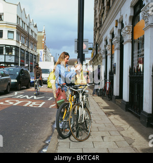 Femme à l'extérieur de l'Épicerie magasin biologique La mise en sacs shopping net sur son vélo Kingsland Road Londres Angleterre KATHY DEWITT Banque D'Images