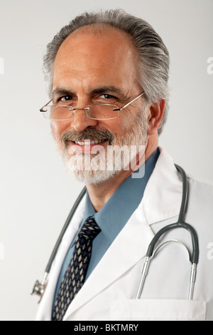 Portrait d'un médecin portant des lunettes et d'un sarrau blanc, avec un stéthoscope drapé autour de son cou. Il est à la recherche à l'appareil photo. Banque D'Images