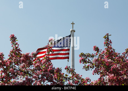 L'église catholique avec une croix et le drapeau américain sur un mât de drapeau avec l'arbre en fleurs contre le ciel bleu angle bas personne horizontal dans l'Ohio USA US h-RES Banque D'Images